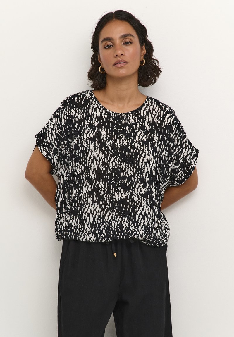Short-sleeve black and white top with a textured abstract pattern, round neckline, and relaxed fit, paired with black pants.
