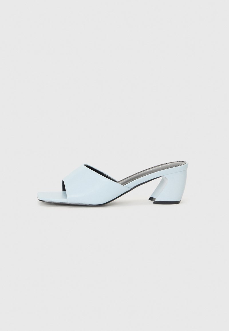 Light blue open-toe heeled mules with a geometric design, featuring a wide strap across the foot and a chunky, angular heel.