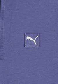 Lilla bomuldsstof med struktureret overflade, med et hvidt Puma-logo på en firkantet lap. Enkel design, uden yderligere mønstre eller accenter.