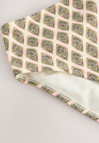 Katoenen stof met een bladpatroon in marineblauw en goud op een lichtroze achtergrond. De randen zijn voorzien van een zachte, gladde witte voering met nette stiknaden.