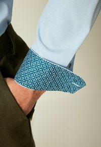Cămașă albastru deschis cu manșetă patterned de teal închis, cu designuri geometrice albe, afișând un material texturat și o croială clasică.