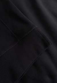 Black fabric close-up featuring smooth and ribbed textures, with visible stitching details. Uniform color without patterns or accents.