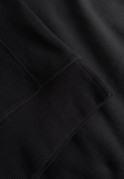 Prim-plan cu țesătură neagră, evidențiind texturi netede și striate, cu detalii vizibile de cusătură. Culoare uniformă, fără modele sau accente.