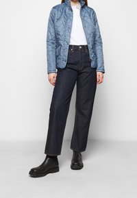 Jasnoniebieska pikowana kurtka z wysokim kołnierzem, zestawiona z ciemnoniebieskimi szerokimi jeansami. Czarne botki za kostkę. Prosty, funkcjonalny design.