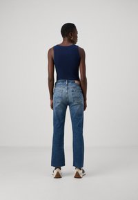 Marinblå ärmlös topp i kombination med högmidjade, blekta jeans i rak passform med rå nederkant. Sportiga skor fulländar looken.