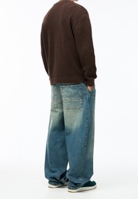 Ruskea ribbineulepaita, löysät haalistuneet siniset farkut suurilla taskuilla ja vihreät kengät. Asussa on rento siluetti ja teksturoitu kangas.