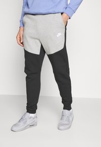 Ljust grå och svarta joggingsbyxor med en avsmalnande design, tillverkade av mjukt material; har en Nike-logotyp på låret och sidofickor.