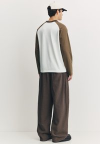 Cămașă cu mânecă lungă, corp albastru deschis și mâneci verde măsliniu, asortată cu pantaloni largi cu carouri maro. Pantofi negri cu talpă groasă.