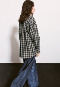 Camasa supradimensionată în carouri navy și crem, cu mâneci lungi și o siluetă relaxată, purtată cu pantaloni din denim oversized.