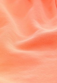 Textielstof in een heldere koraalkleur, met een gladde, gestructureerde oppervlakte en een subtiel patroon van kleine, verhoogde stippen overal.