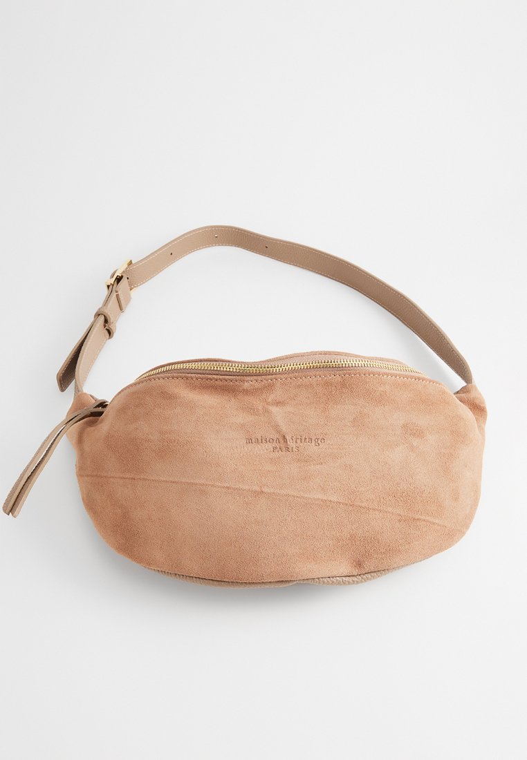 Banane en suède beige avec une texture lisse, une forme arrondie, une fermeture éclair, des éléments en or et le nom de la marque embossé à l'avant.