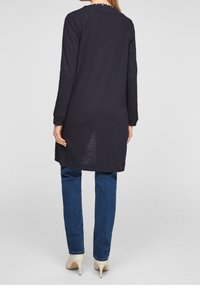 Marinblå långärmad tunika med rund halsringning, lätt tyg och sidofickor. Kombinerad med blå denimjeans och krämfärgade klackar.