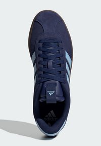 Marinblå mockaskor med ljusblå ränder, texturerad ovandel, vadderat krage och brun gummisul. Varumärke vid häl och tunga.