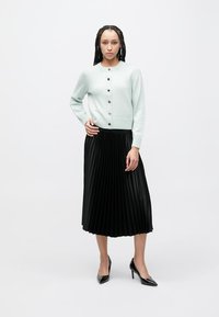 Light blue cardigan with gold buttons, paired with a black pleated skirt and black heels, showcasing a clean, structured design.