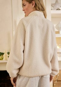 Cremfarbener Fleece-Pullover mit hohem Kragen, lässiger Passform und weicher, strukturierter Oberfläche. Verfügt über gesammelte Ärmelbündchen und einen abgerundeten Saum.