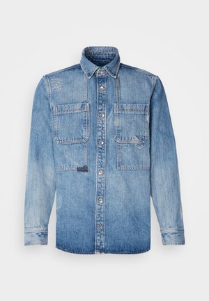 Light blue denim shirt with long sleeves, button closure, two chest pockets, and subtle distressed details. Smooth texture with a classic cut.