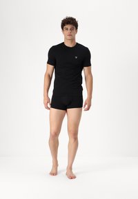 Svart, tettsittende T-skjorte og matchende boxershorts laget av et glatt materiale. T-skjorten har en liten logo på brystet.