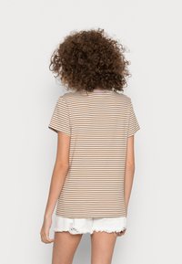 T-shirt listrado em tons de bege e creme, com mangas curtas, decote redondo, feito de tecido suave. Usado com calções brancos desgastados.