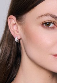 Srebrne kolczyki w formie obręczy z teksturowaną powierzchnią i błyszczącymi akcentami, spoczywające na małżowinie usznej, prezentujące polerowane wykończenie.