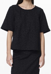 Woman wearing a black textured short-sleeve top and matching skirt with a subtle heart pattern on a plain white background.