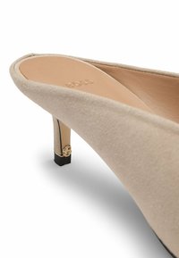 Beige suede mid-heel shoe with a pointed toe, gold accent on the heel, and a smooth leather interior. Elegant design with minimal texture.