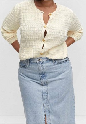 Personne portant un cardigan crème texturé boutonné avec des manches retroussées et une jupe en denim bleu clair taille haute avec une fente à l'avant.