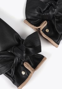 Black leather gloves featuring large black bows at the wrists, with a contrasting beige trim and a brass snap detail.