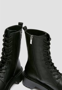 Czarne botki za kostkę z sznurowanym przodem, suwakami po bokach i grubą podeszwą. Wykonane z gładkiego materiału syntetycznego o matowym wykończeniu.