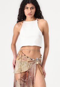 White cropped tank top paired with a sheer, multi-colored skirt featuring a geometric pattern, accentuated by a beaded belt.