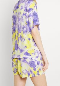 Completo da loungewear multicolore composto da una maglietta a maniche corte e pantaloni corti in giallo e viola, con un motivo tie-dye e una texture morbida.