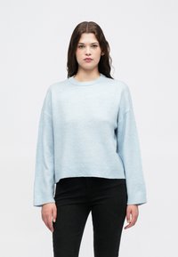 Lys blå genser med rund hals, ribbestrikkede mansjetter og avkortet kant. Laget av mykt materiale med en lett strukturert overflate.