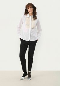 White button-up shirt with a textured cream panel featuring sequins. Paired with black tapered trousers and silver pointed-toe heels.