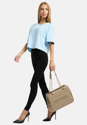 Kort lyseblå T-shirt med grafisk detalje, sorte leggings, sorte stiletter og en beige quiltet håndtaske med kæderemme.