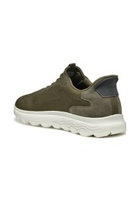 Zapatilla deportiva verde oliva con parte superior de punto texturizado, acentos de ante y suela de goma blanca con un patrón de olas.