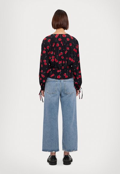 Blusa nera a maniche lunghe con stampa di ciliegie rosse, vita elastica e coulisse alle maniche, abbinata a jeans a gamba larga di colore blu chiaro e scarpe nere.