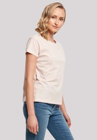 T-shirt en coton rose clair à manches courtes, col rond et coupe décontractée, associé à un jean en denim bleu.