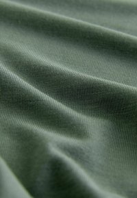 Gros plan sur un tissu vert avec une texture côtelée fine visible et des plis doux créant des ombres délicates.