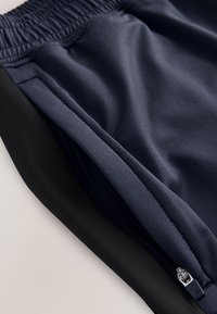 Nahaufnahme von marineblauen und schwarzen Hosen mit elastischem Bund und sichtbarem Metallreißverschluss an der marineblauen Seitentasche.