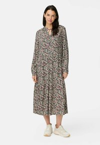 Florale midi-jurk op een donkere achtergrond met roze en witte bloesems, lange mouwen, striknek en een geraffineerde taille, gecombineerd met witte sneakers.