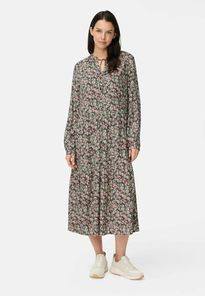 Florales Midikleid auf dunklem Hintergrund mit rosa und weißen Blüten, langen Ärmeln, gebundenem Kragen und gerafftem Taillenteíl, kombiniert mit weißen Sneakers.