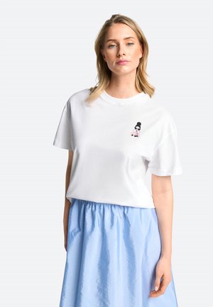 White cotton t-shirt featuring a small graphic design on the left chest area. Worn with a light blue, gathered skirt.