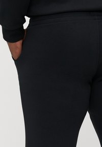 Schwarze Sporthosen aus weichem Stoff, mit einem elastischen Bund und seitlichen Taschen, gleichmäßig und glatt in der Textur.