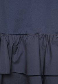 Tissu bleu marine foncé avec détail de volants froncés et superposés, montrant la texture et les coutures sur un vêtement.