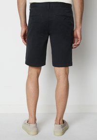 Mörkblå shorts i lätt material, med en rak front, bakfickor och rak passform, som är parat med ljusa skor.