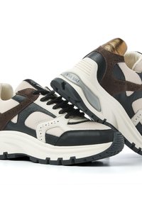 Chunky sneakers with beige mesh, black and brown leather panels, black laces, thick white soles, and gold metallic accents on the heel.