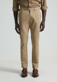 Chinos beige con un corte recto, que cuentan con bolsillos frontales y passacinturones, combinados con zapatos de cuero marrón. Tejido suave y ligero.