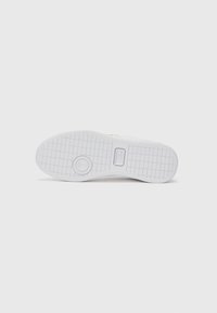 Hvit sneakersåle med et teksturert grep mønster, med en sirkulær detalj og rektangulær merkevareføring, på en ensfarget bakgrunn.