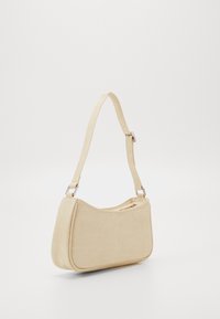 Vaaleanbeige nahkainen olkalaukku, jossa on teksturoitu pinta, kaareva muoto ja säädettävä olkahihna, jossa on hopeiset yksityiskohdat. Vetoketjullinen pääosasto.