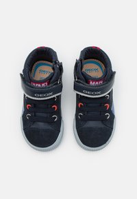 Zapatillas azul marino con parte superior de ante y textil, suela de goma gris, ojetes naranjas, correa y logotipo de Marvel en la correa del tobillo.