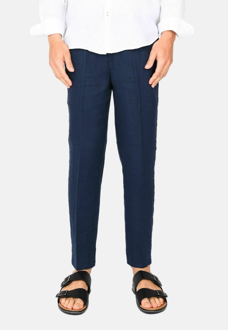 Pantaloni di lino blu navy con una vestibilità slim e pieghe frontali sottili, abbinati a sandali neri con doppie cinghie e suole testurizzate.
